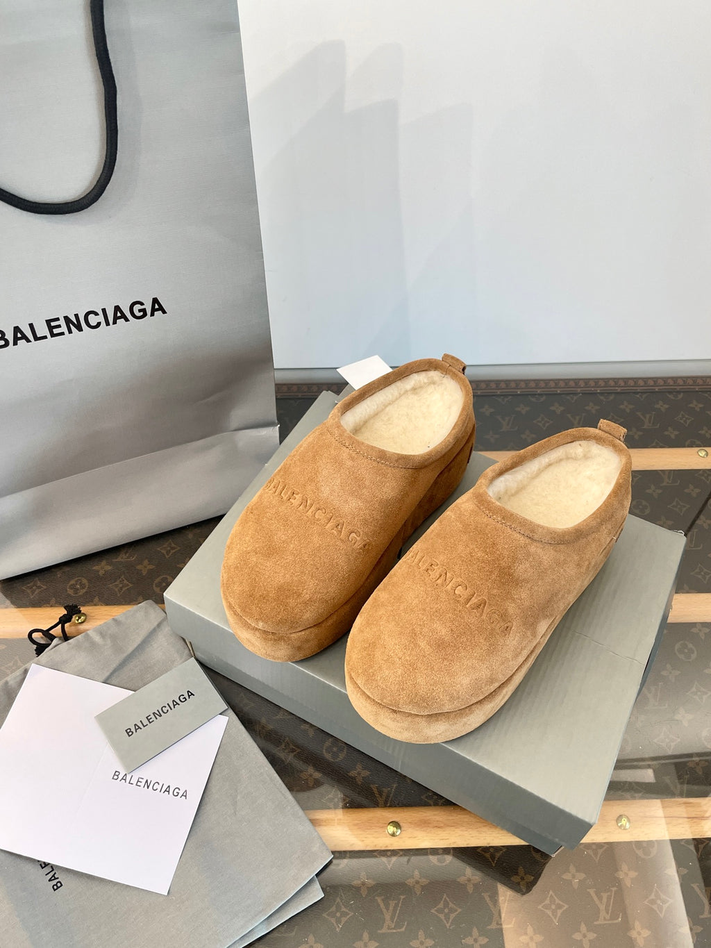 Tan suede slip-on sandals with beige lining, pair on a shoebox with paper inserts.
