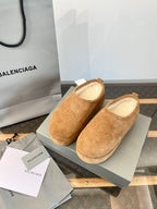 Tan suede slip-on sandals with beige lining, pair on a shoebox with paper inserts.