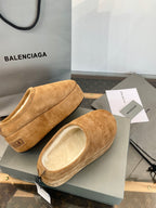 Tan suede slip-on sandals with beige lining, side and front angles on a gray box lid.