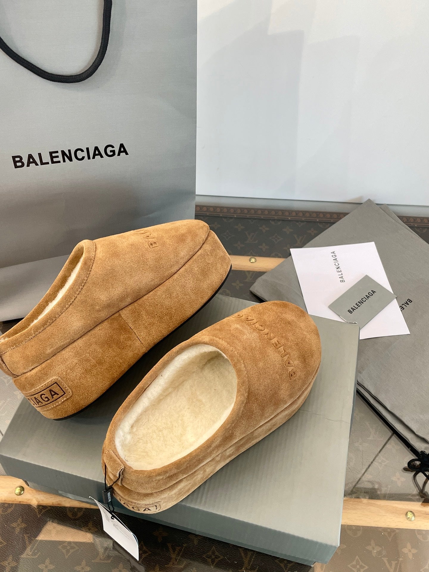 Tan suede slip-on sandals with beige lining, side and front angles on a gray box lid.