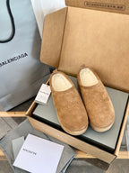 Tan suede slip-on sandals with beige lining, pair displayed in an open shoebox.