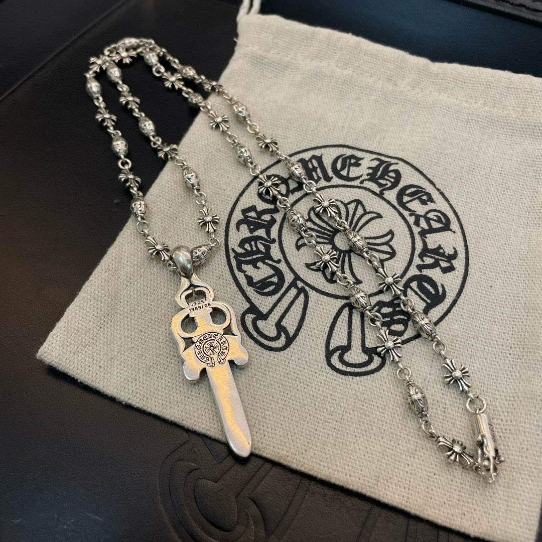 Silver-tone necklace with sword pendant and flower-studded chain on cloth pouch