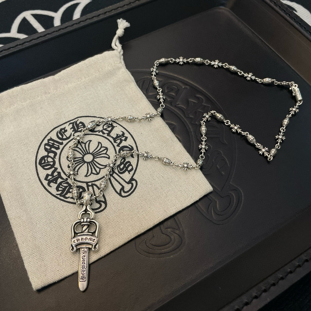 Silver-tone necklace with sword pendant and floral chain links on a cloth pouch