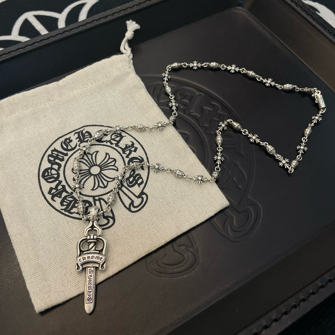 Silver-tone necklace with sword pendant and floral chain links on a cloth pouch