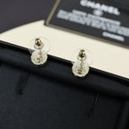 Gold-tone stud earrings with circular CC logo, shown from the back on dark fabric.