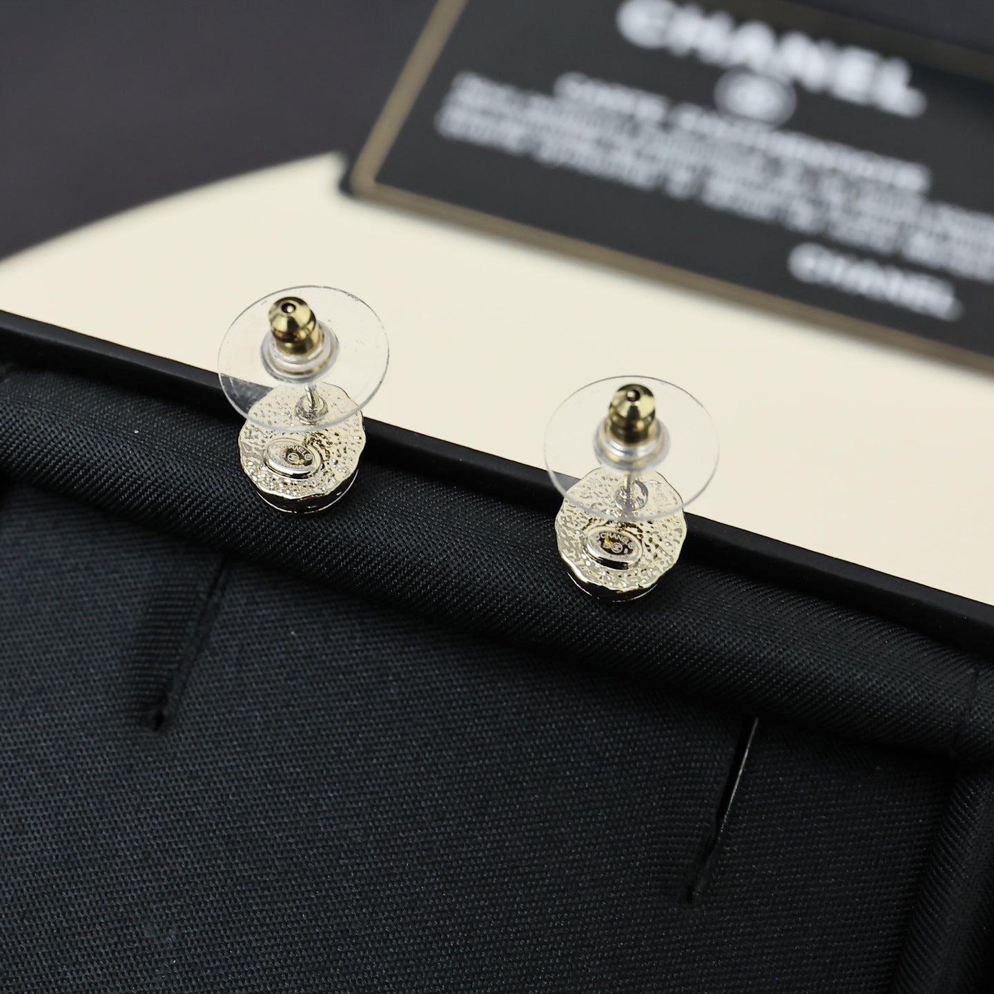 Gold-tone stud earrings with circular CC logo, shown from the back on dark fabric.