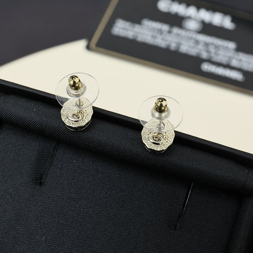 Gold-tone stud earrings with circular CC logo, shown from the back on dark fabric.