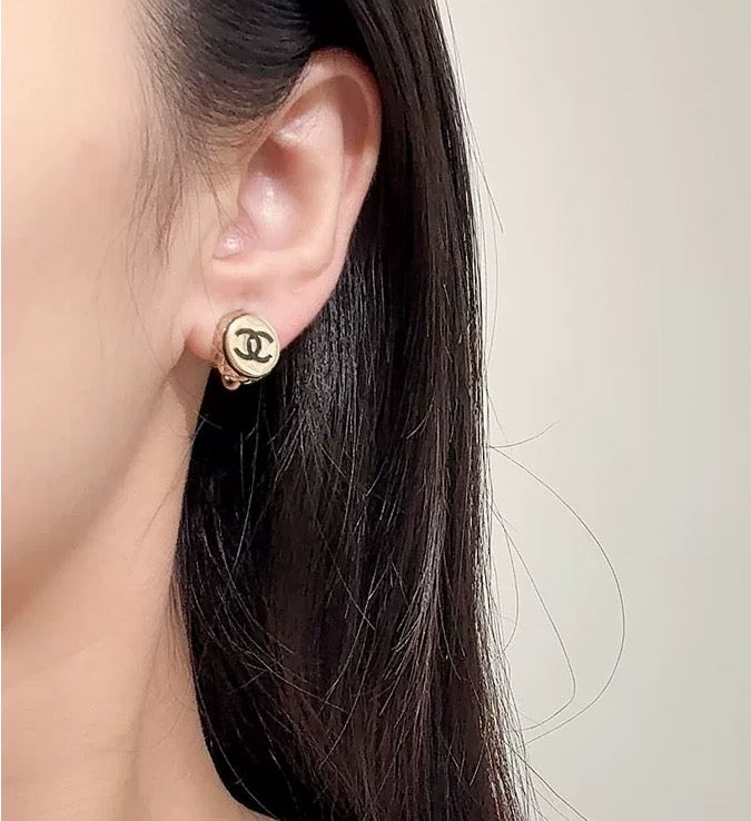 Gold-tone circular CC stud earring on ear, angled side view.