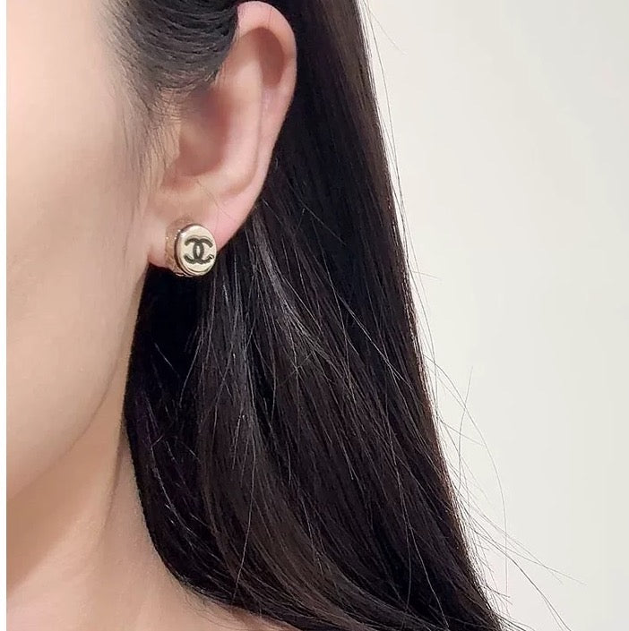 Gold-tone circular CC stud earring on ear, close-up view.