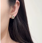 Gold-tone circular CC stud earring on ear, close-up view.