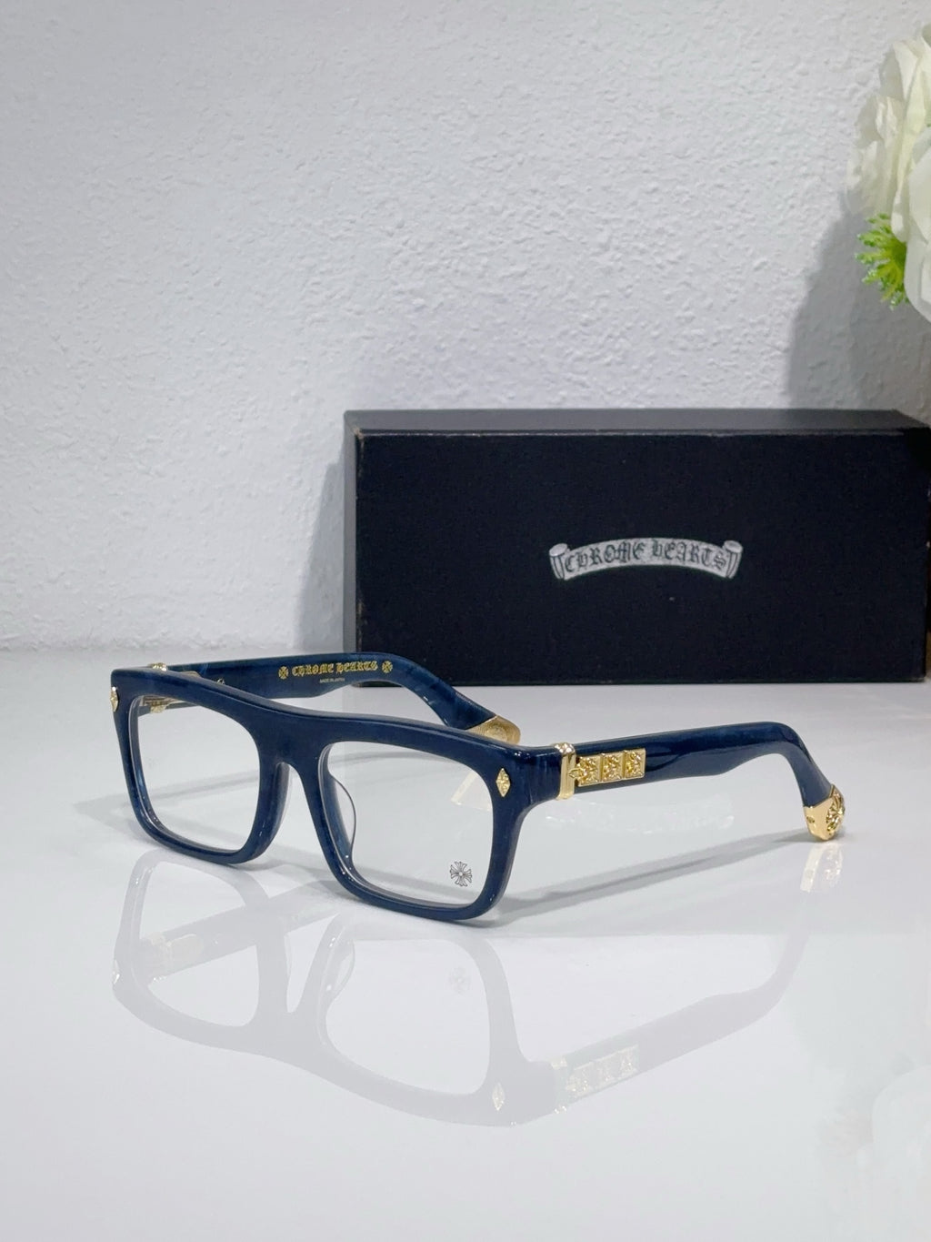 Rectangular eyeglasses with dark blue frames and gold temple logo accents
