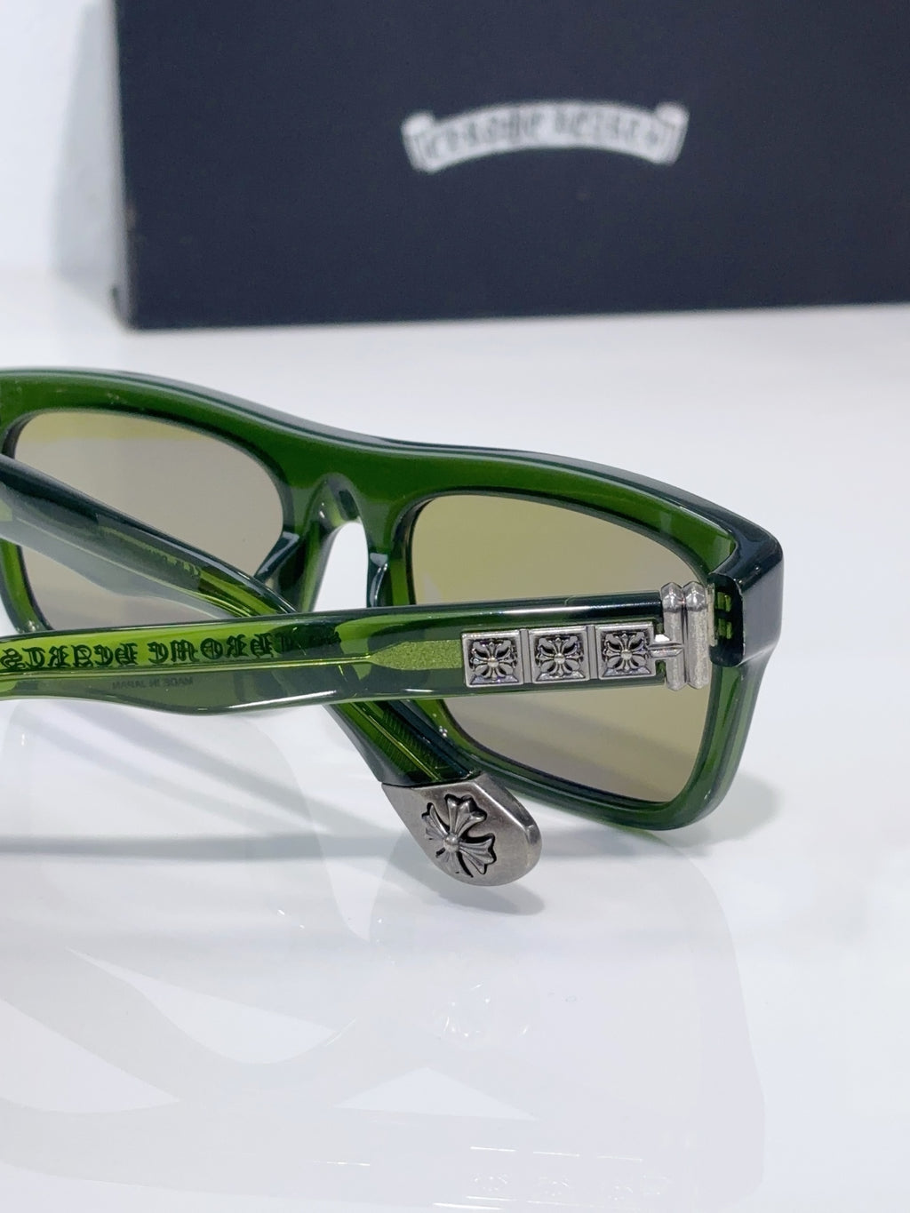 Chrome glasses close-up, green frames with decorative center bar and tan-tinted lenses
