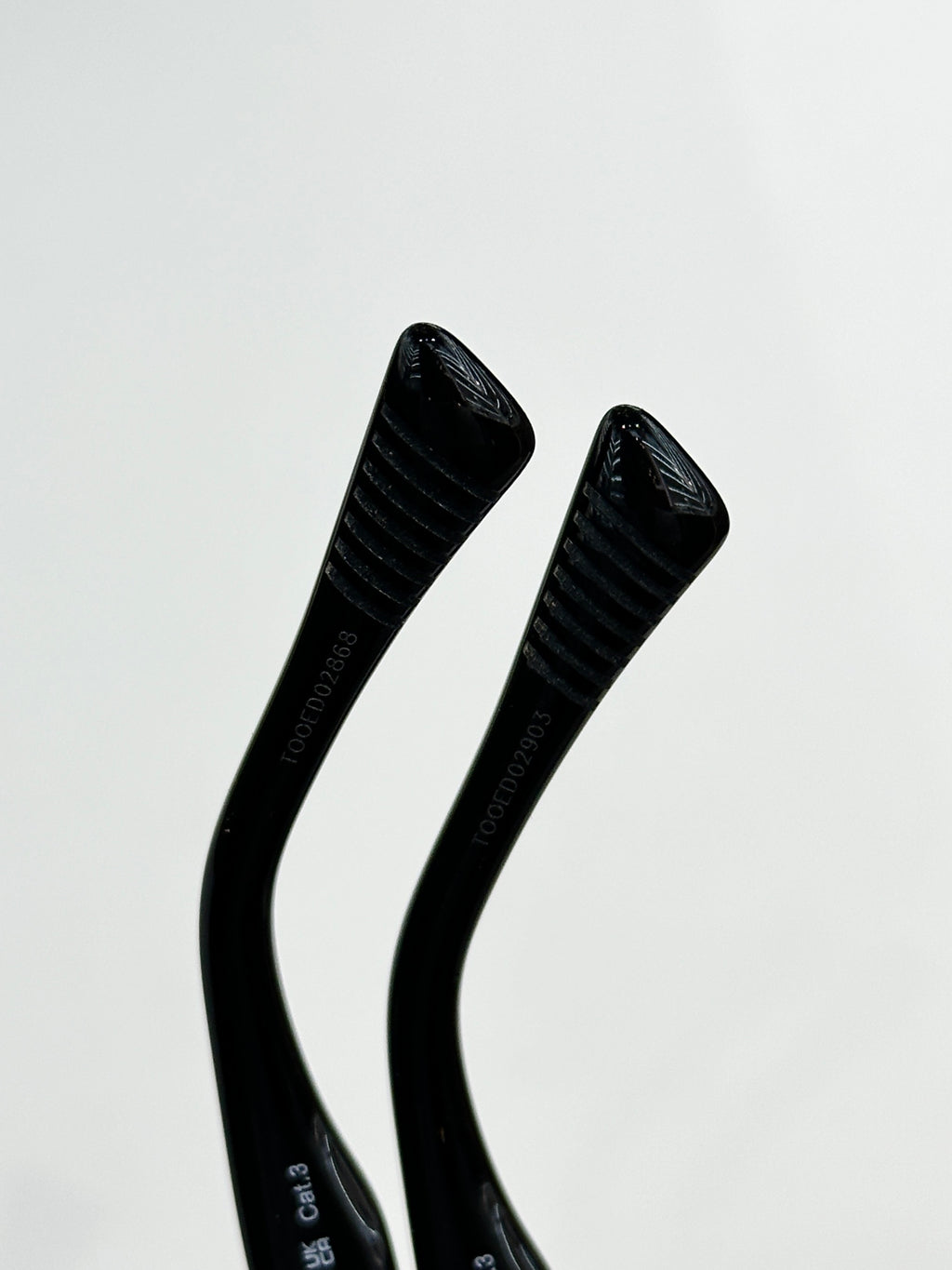 Sunglasses temple close-up with black ribbed arms and embossed logo text.