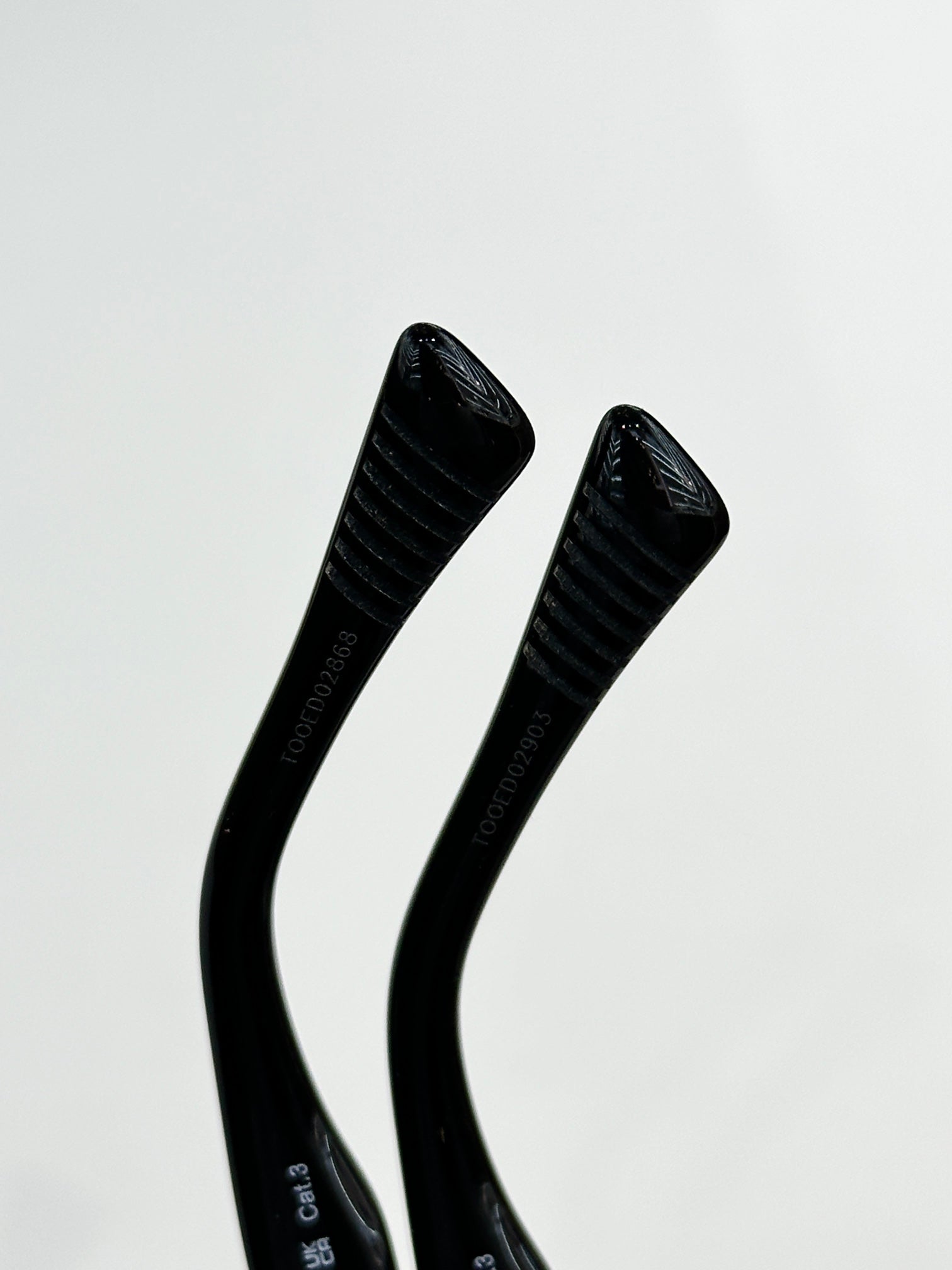Sunglasses temple close-up with black ribbed arms and embossed logo text.