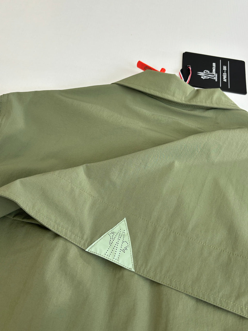 Long olive coat with hem label and triangular mesh underlayer