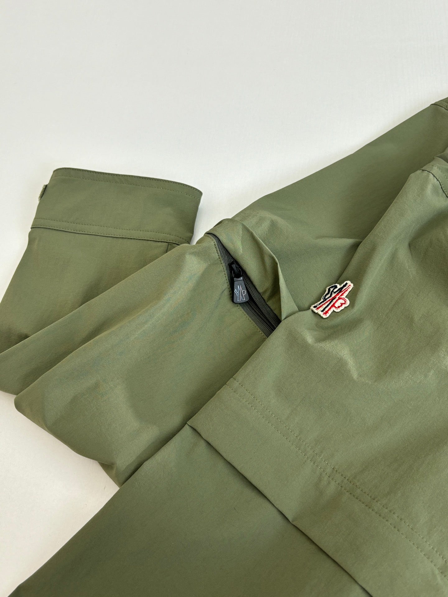 Long olive coat with snap front and red-and-white logo patch on chest