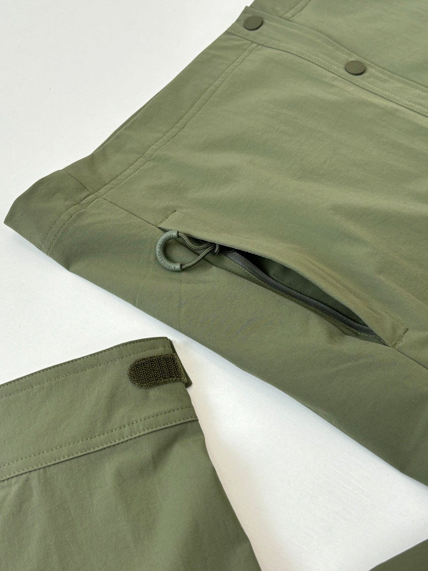 Moncler long jacket in olive green with side flap, snap button, and hem tab