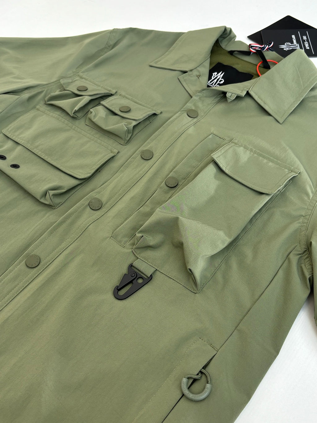 Moncler long jacket olive green front close-up with utility pockets and ring pull