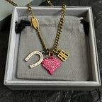 Gold-tone necklace with pink heart and horseshoe charms, shown in jewelry box
