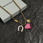 Gold-tone chain necklace with pink heart charm and horseshoe charm, beside box