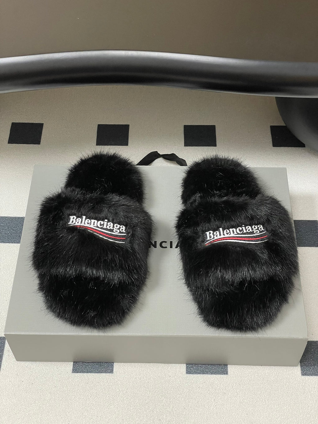 Black fuzzy slide sandals with Balenciaga logo bands, pair shown on display