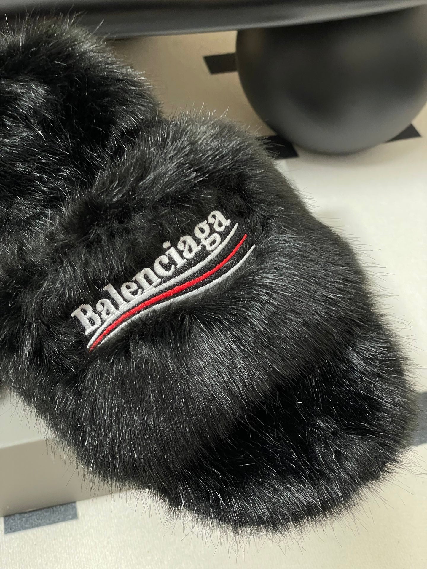 Black faux-fur slide sandal close-up, Balenciaga logo stripe on top band