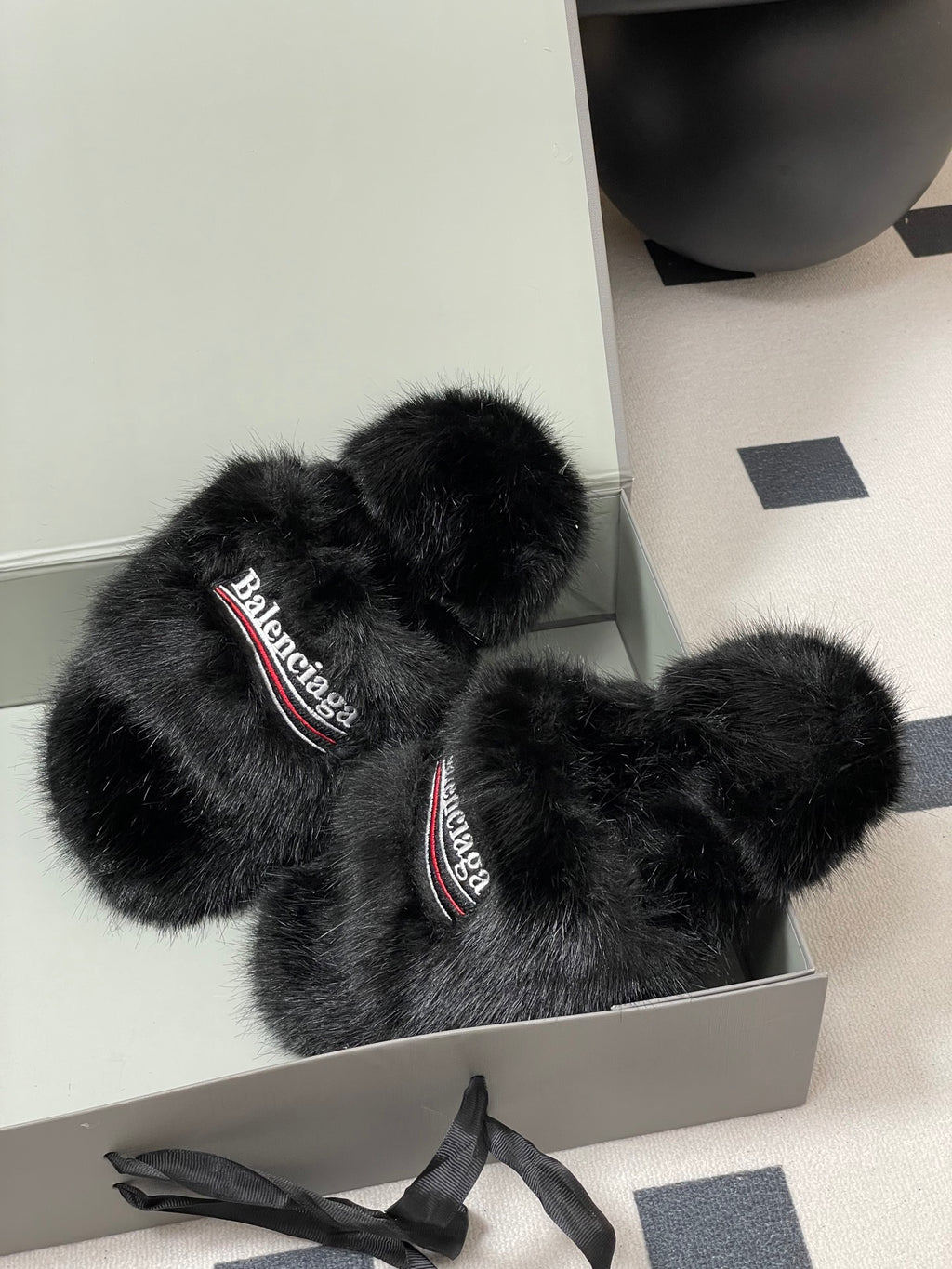 Black fuzzy slide sandals with Balenciaga logo straps, placed in open box