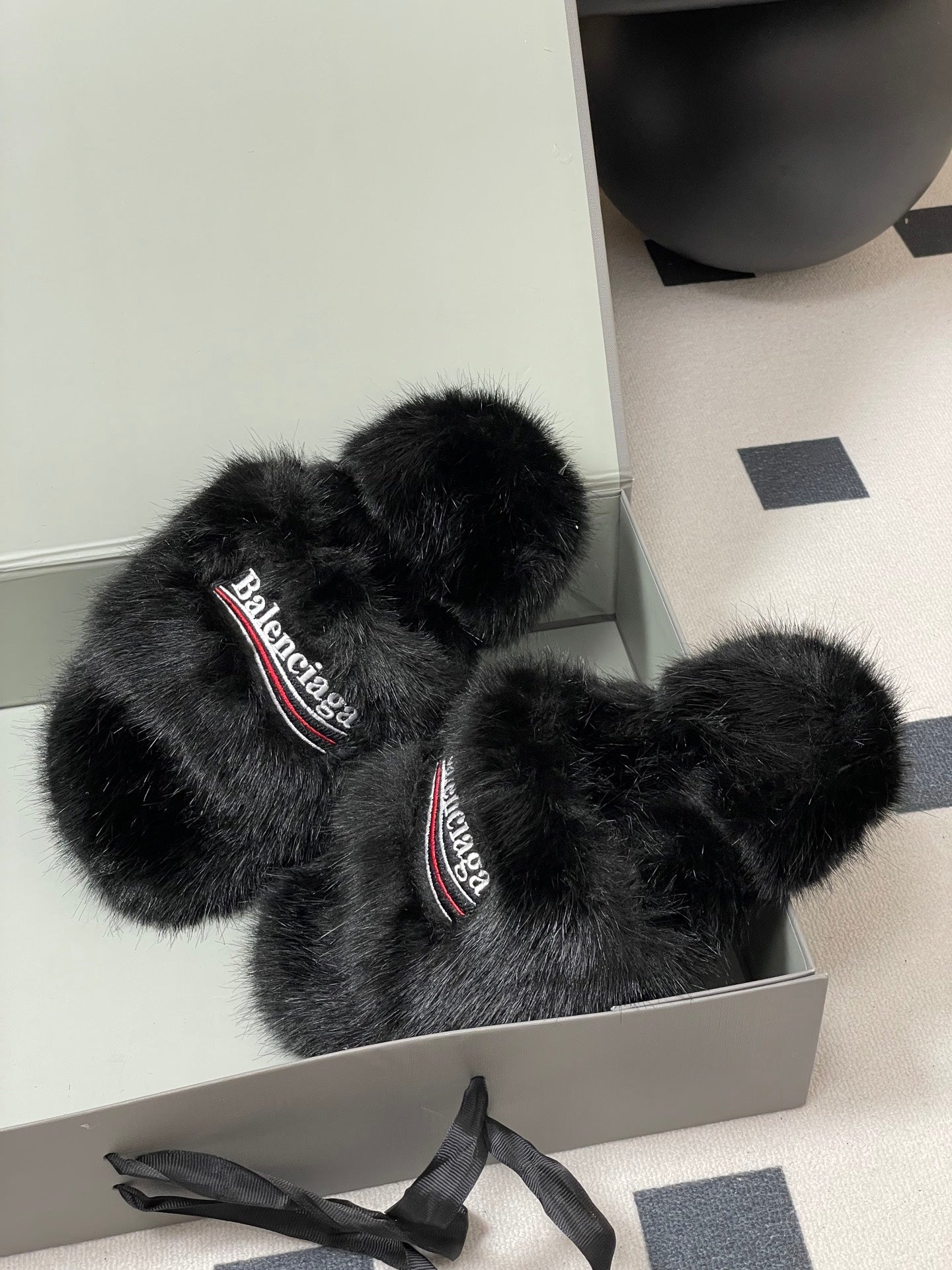 Black fuzzy slide sandals with Balenciaga logo straps, placed in open box