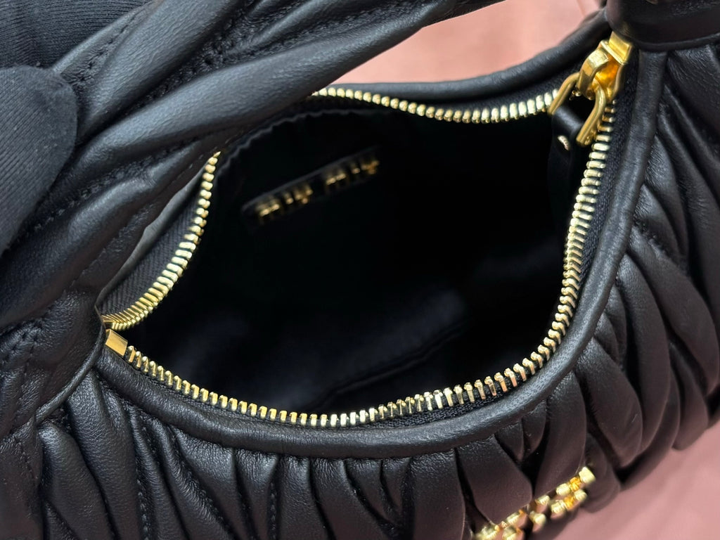 Black leather handbag interior view with gold zipper and ruched edges along the opening