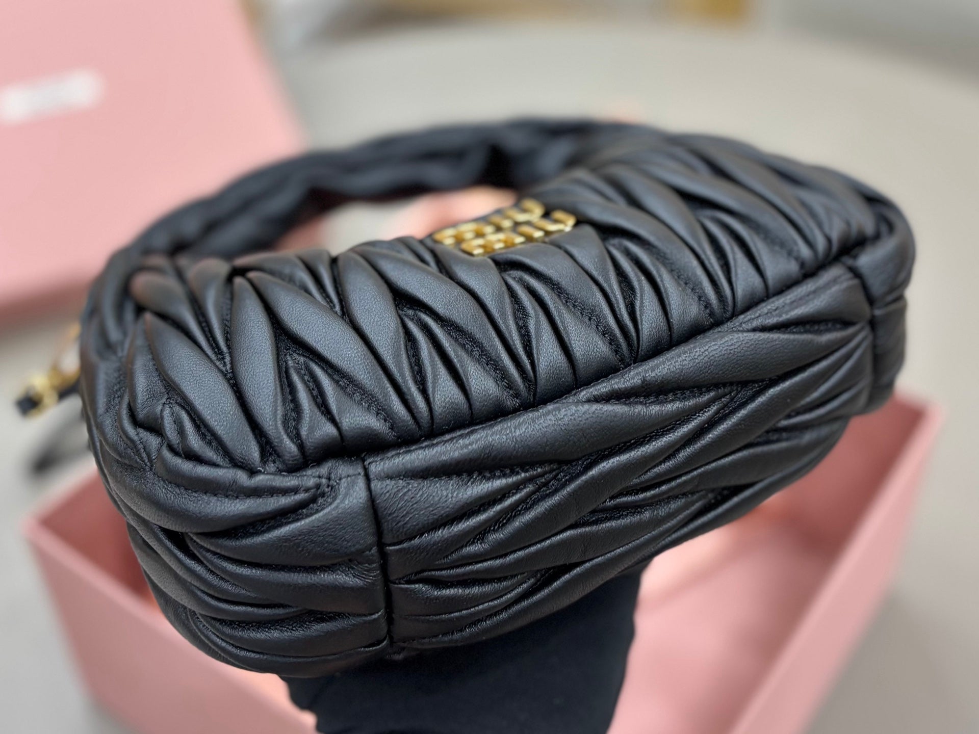 Rolled black leather handbag with ruched quilting, gold clasp hardware, and top handle detail