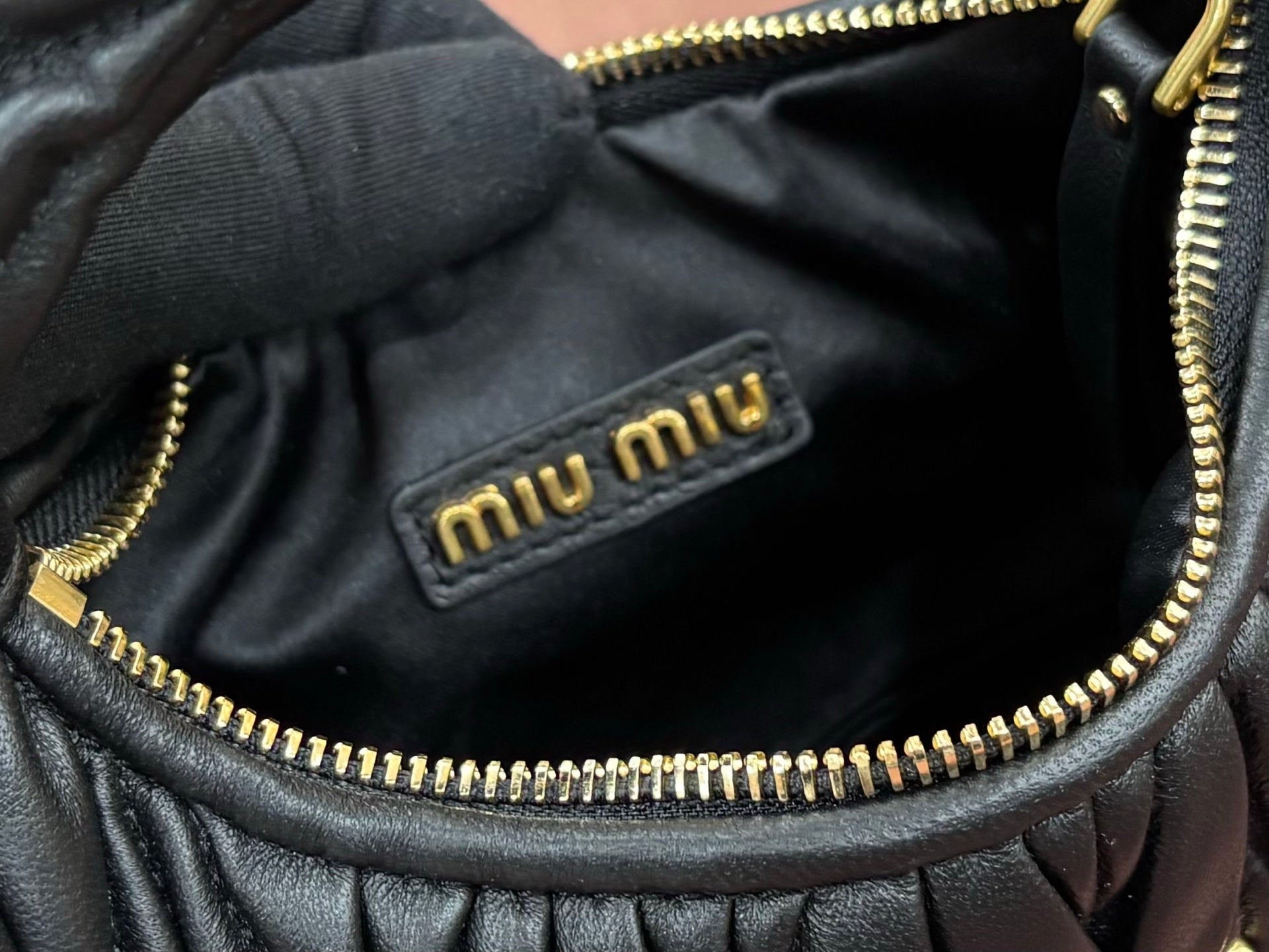 Black leather handbag interior with gold zipper trim and Miu Miu logo patch