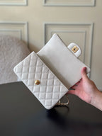 White quilted mini handbag held in hand with flap and gold snap clasp