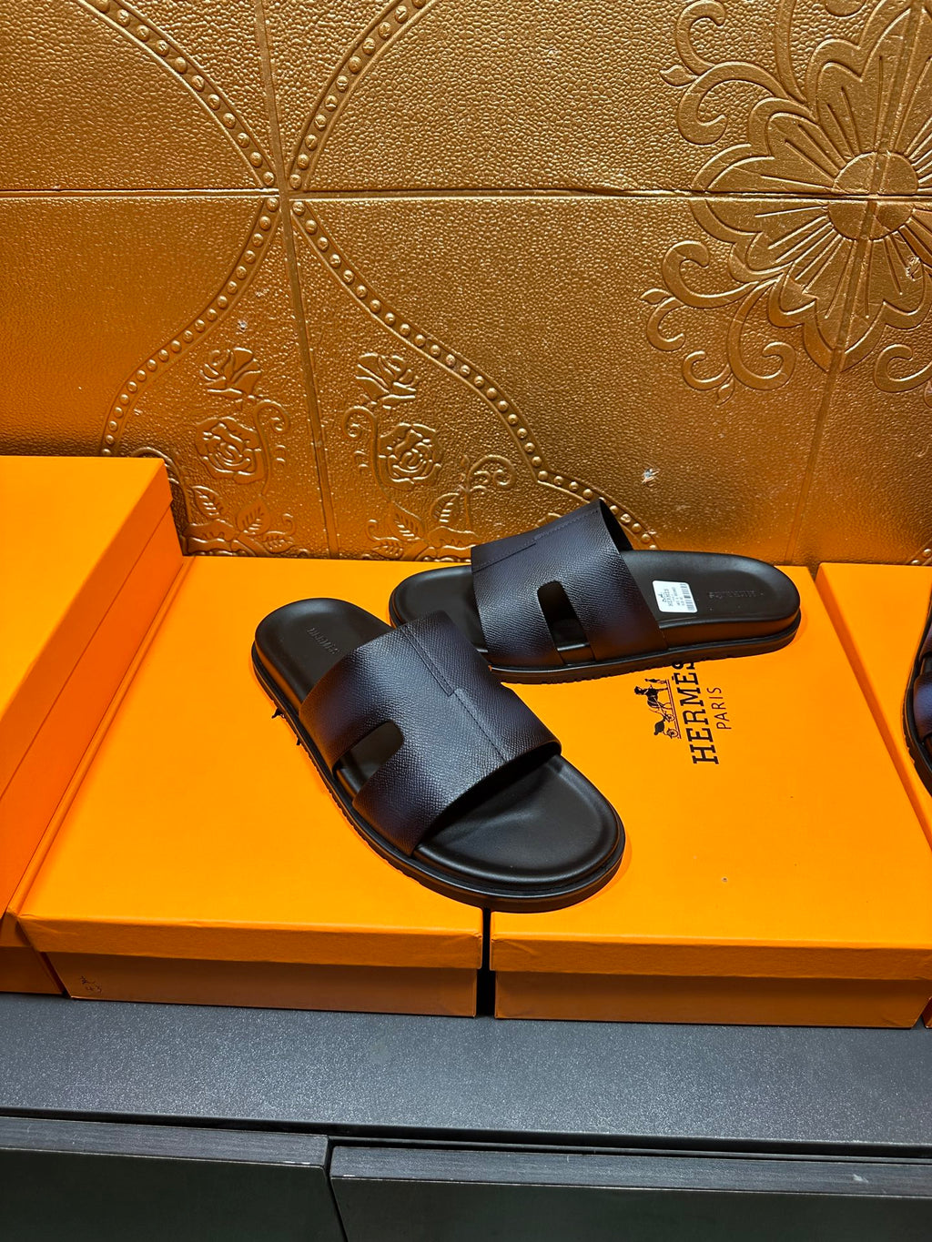 Hermes dark leather slide sandals with wide strap and open toe, on display
