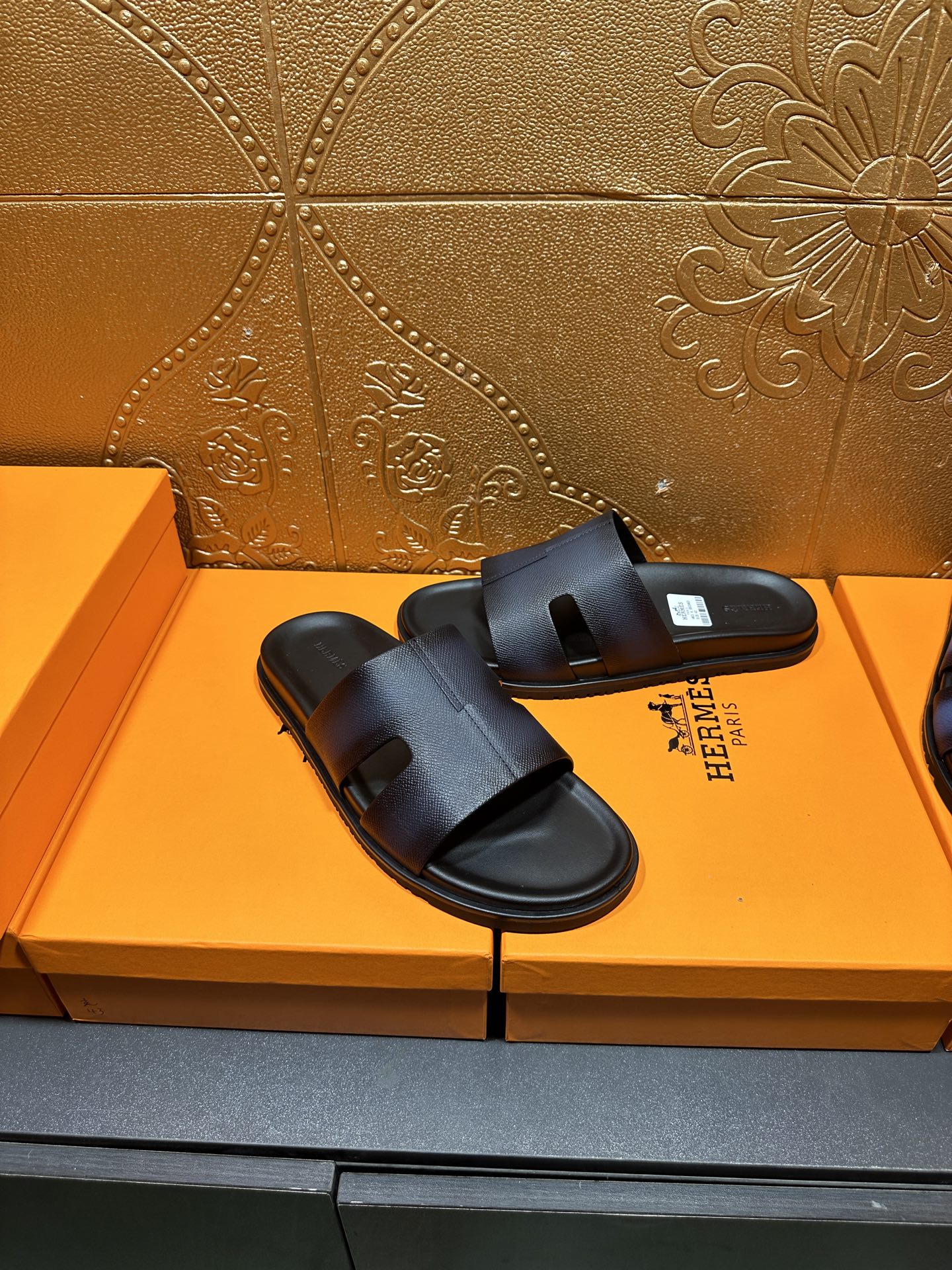 Hermes dark leather slide sandals with wide strap and open toe, on display