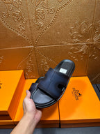 Hermes dark blue leather slide sandal held in hand, side angle with strap