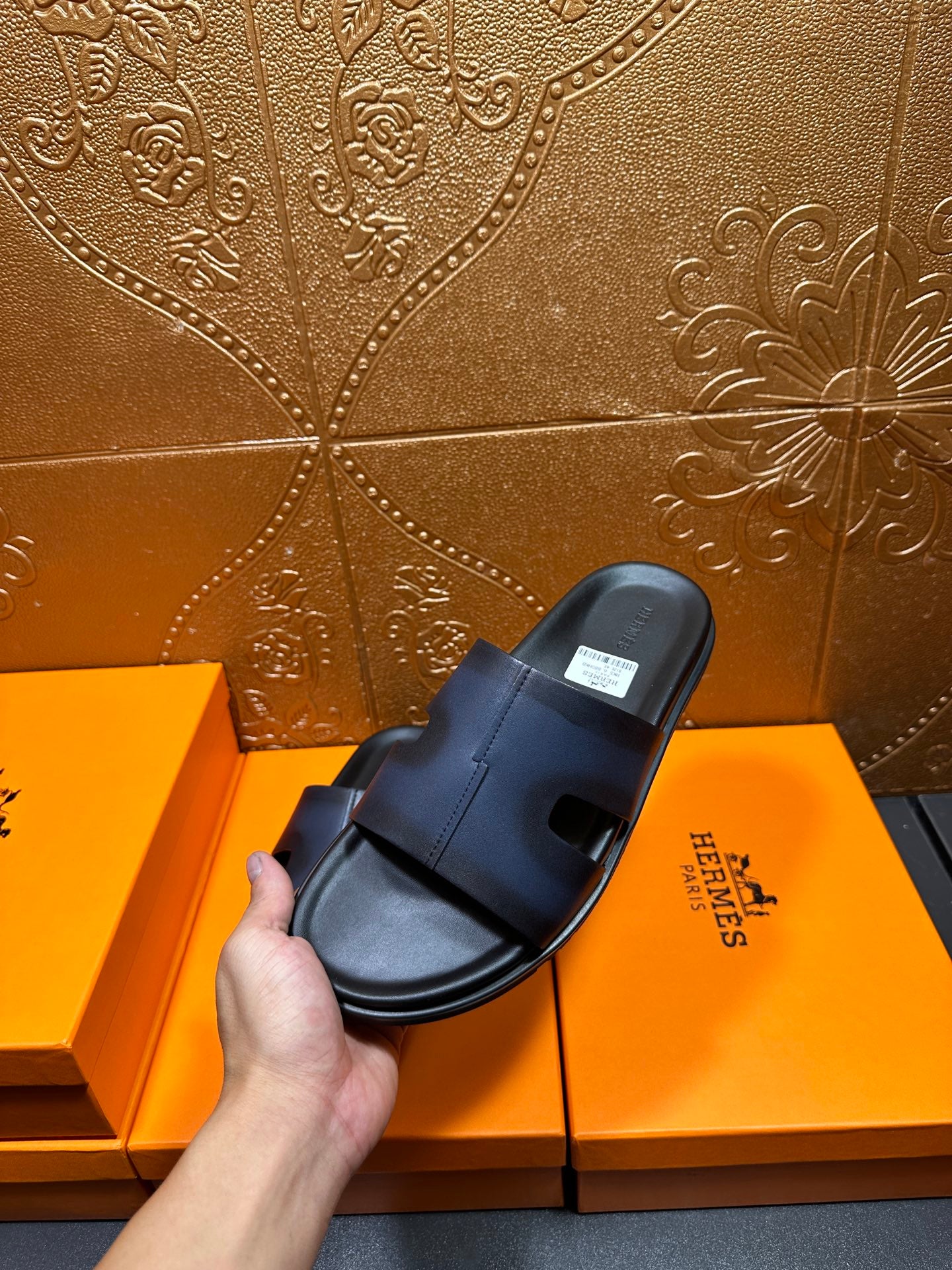 Hermes dark blue leather slide sandal held in hand, side angle with strap
