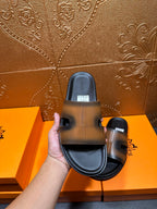Hermes slide sandals held by hand, gray-tan upper with dark sole