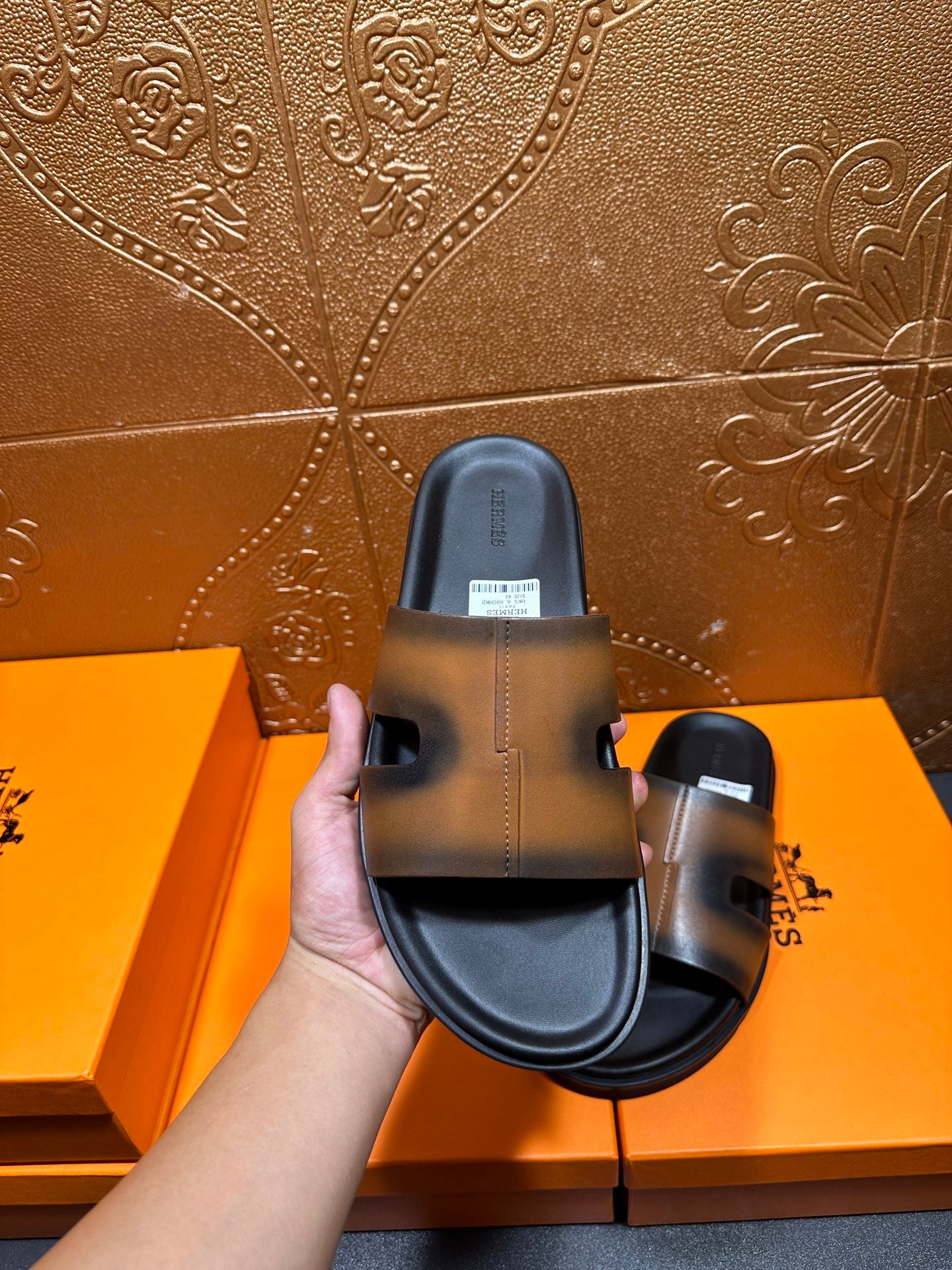Hermes slide sandals held by hand, gray-tan upper with dark sole