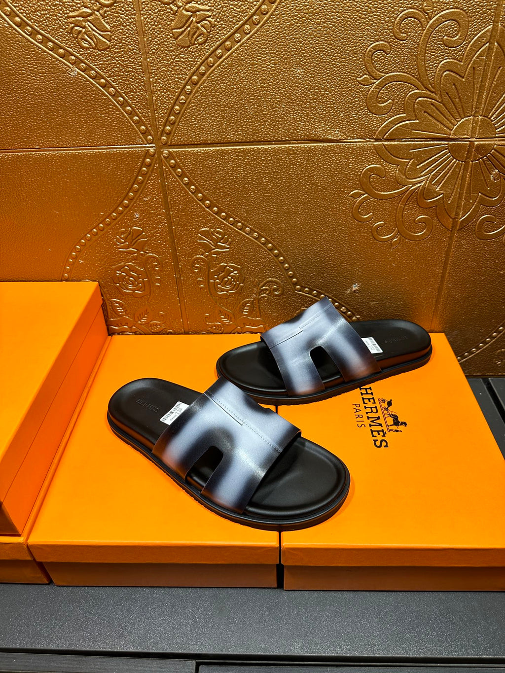 Hermes slide sandals on orange box, metallic blue strap and black sole pair