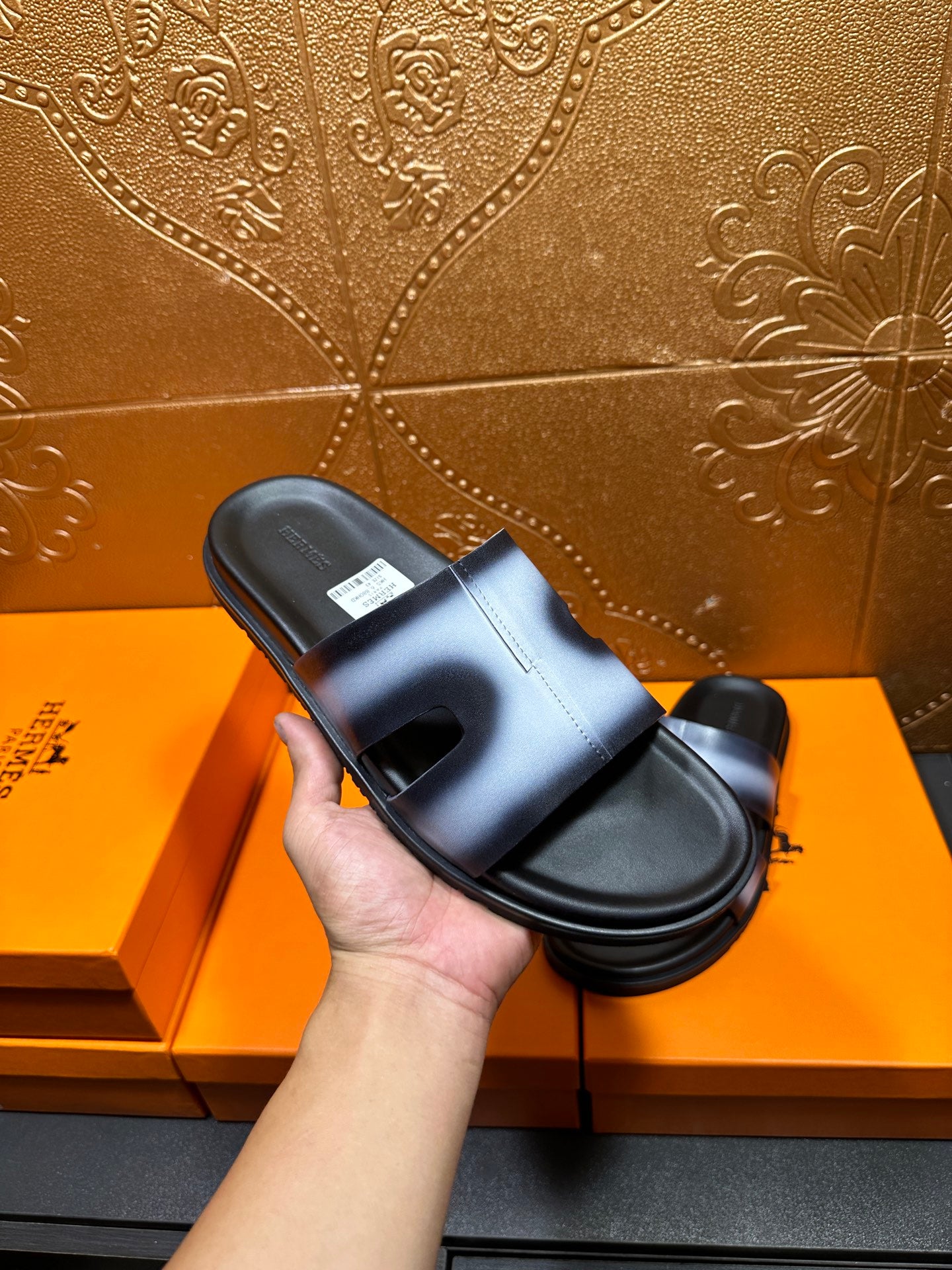 Hermes slide sandal in hand, metallic blue strap over black footbed