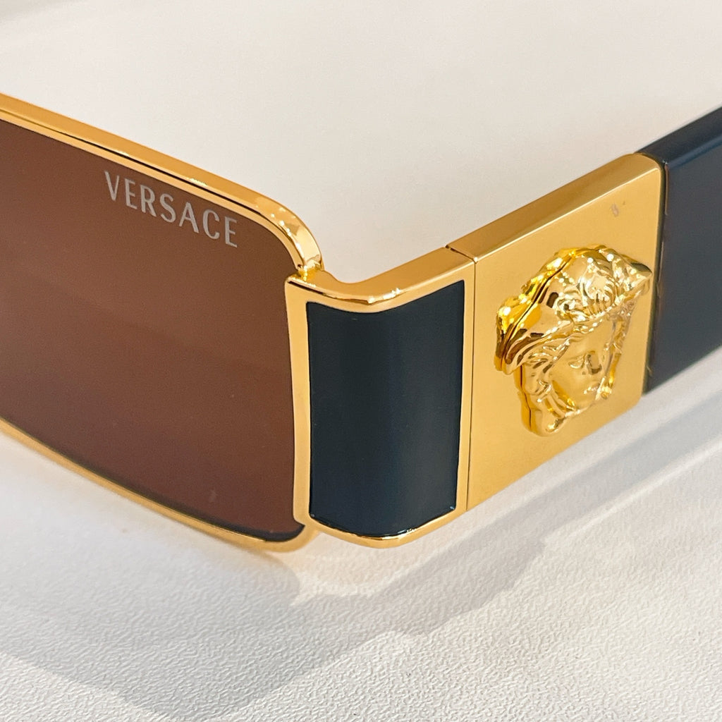 Versace rectangular sunglasses close-up, gold frame, dark lenses, Medusa temple emblem