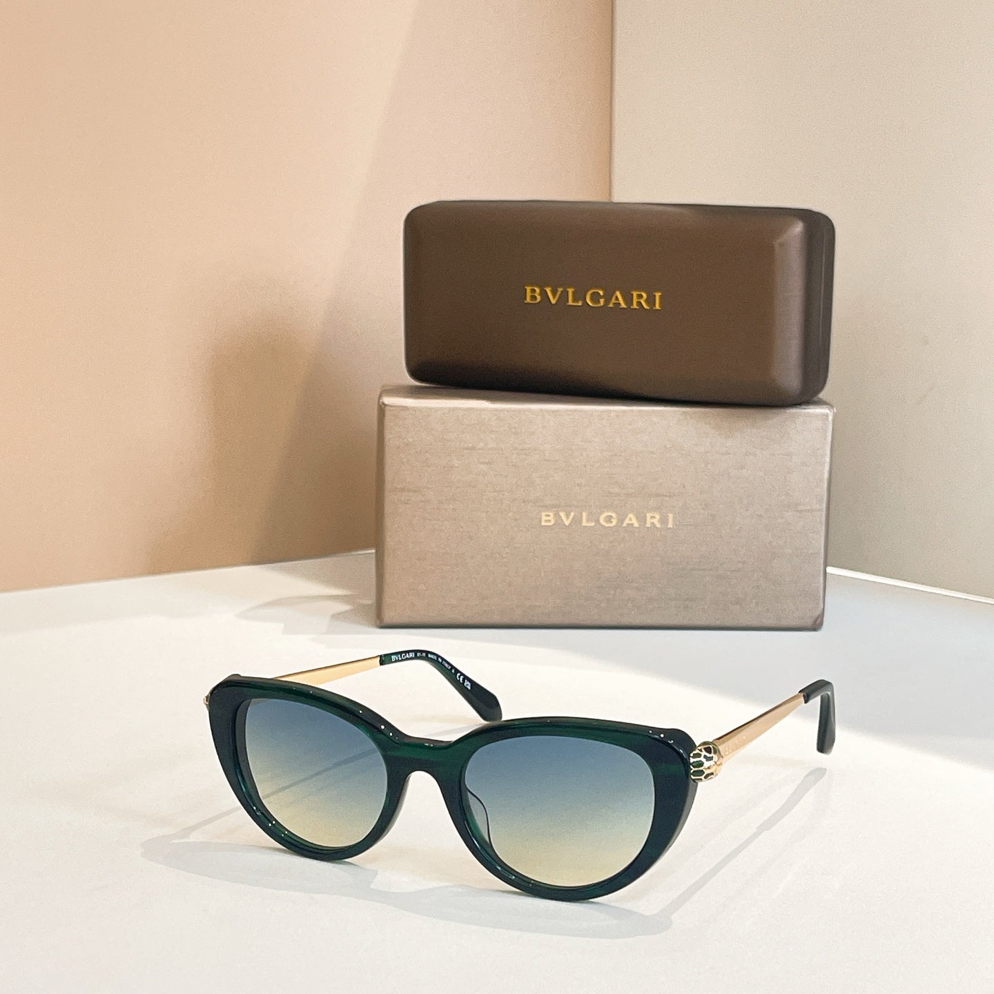 Bvlgari sunglasses with dark green frames and blue-tinted oval lenses, gold-tone detail