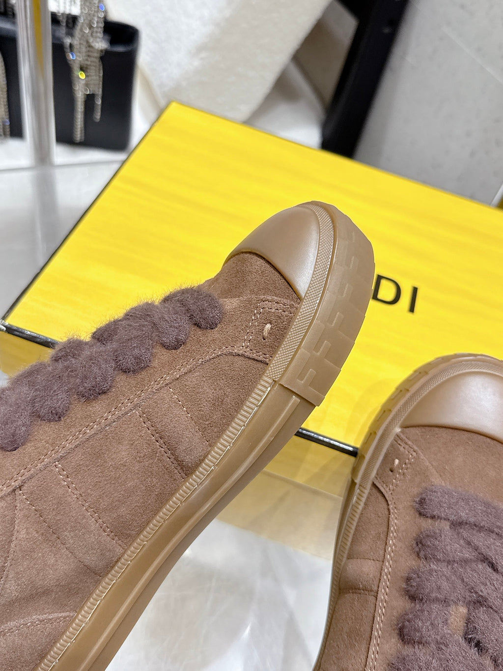 Close-up of brown suede sneaker side with fuzzy lace trim and embossed logo