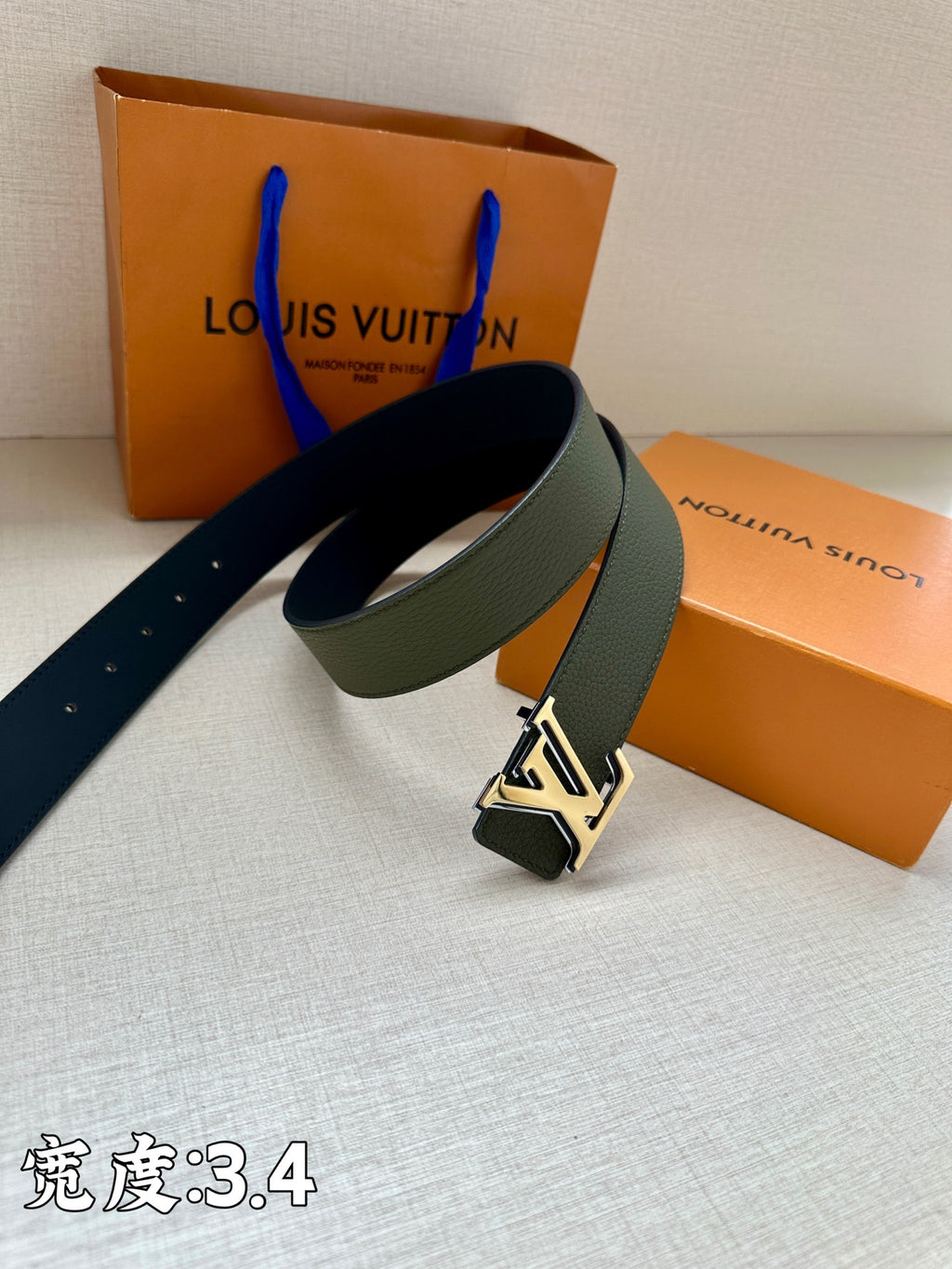Dark green leather belt with large silver logo buckle and eyelet holes
