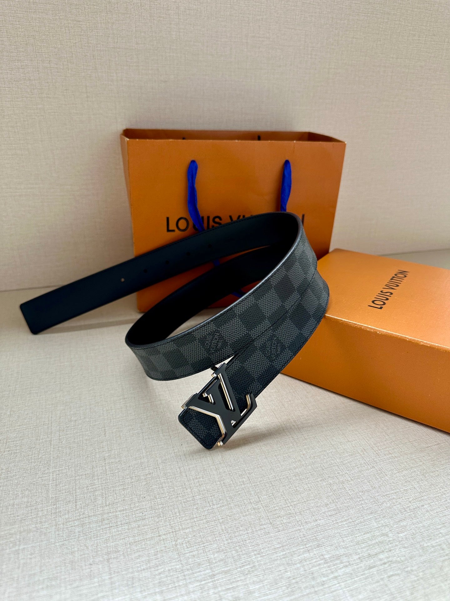 Monogram belt with dark blue check strap and gold-tone buckle, strap across surface