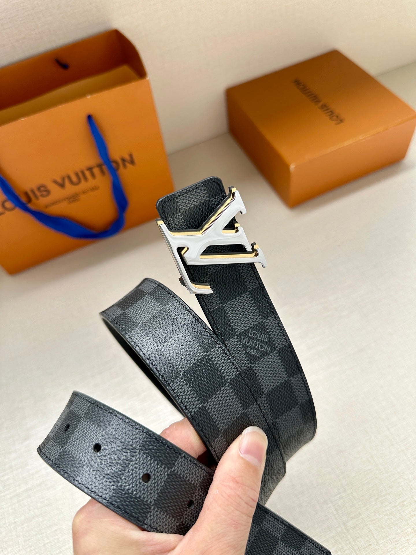 Monogram belt held in hand, dark blue check strap with gold-tone buckle and holes
