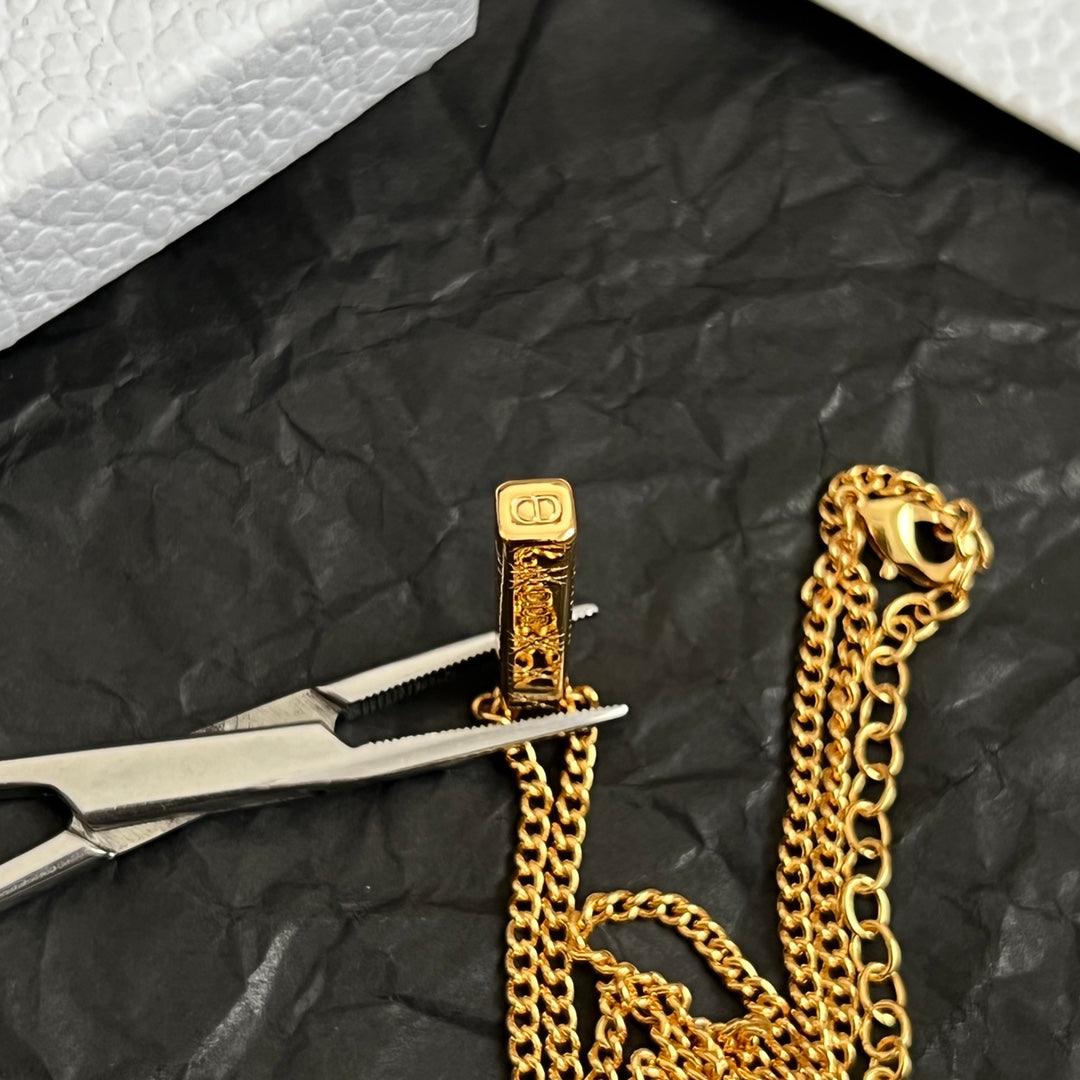 Gold-tone charm detail with bar pendant and intertwined chain links