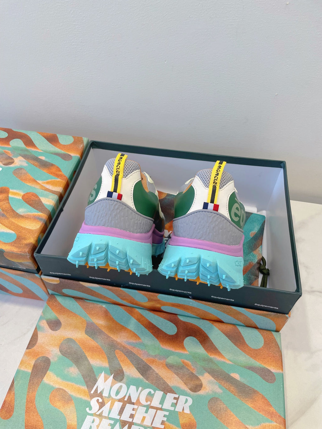Moncler sneakers from back: white-gray uppers, green heel panel, bright blue tread sole
