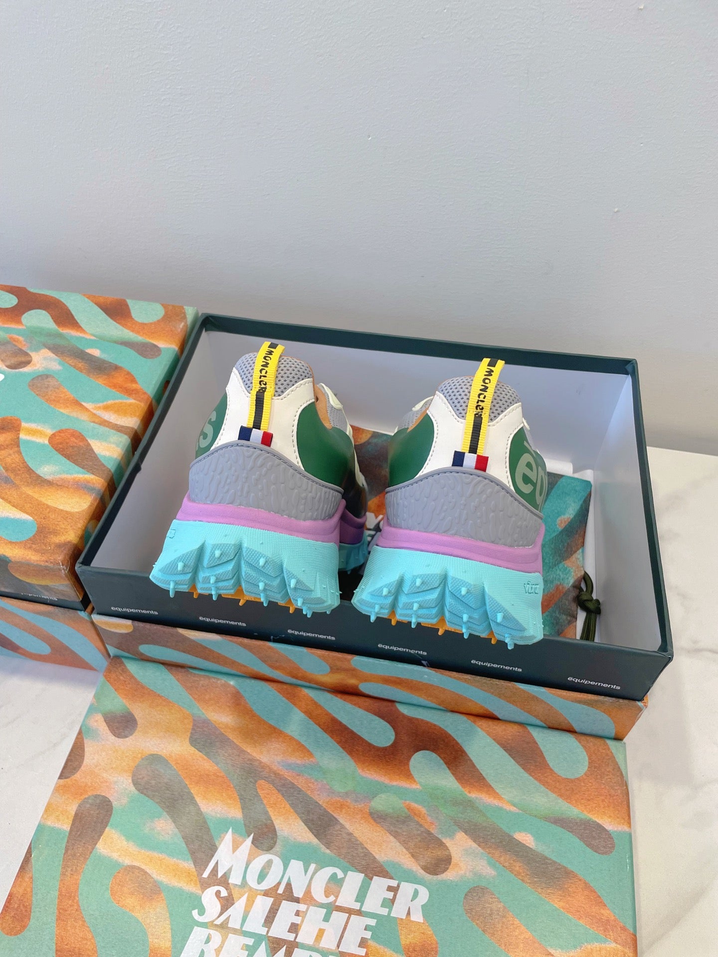 Moncler sneakers from back: white-gray uppers, green heel panel, bright blue tread sole