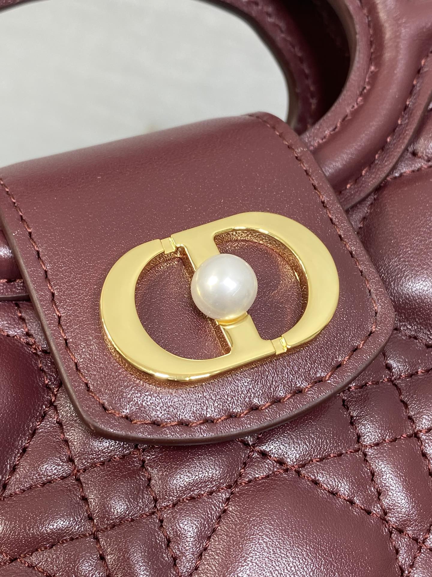 Maroon quilted handbag flap detail with gold circular clasp and white pearl accent
